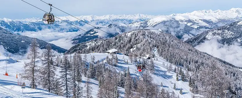 Zasnežena gorska pokrajina s smrekami in žičnico v zimskem času.