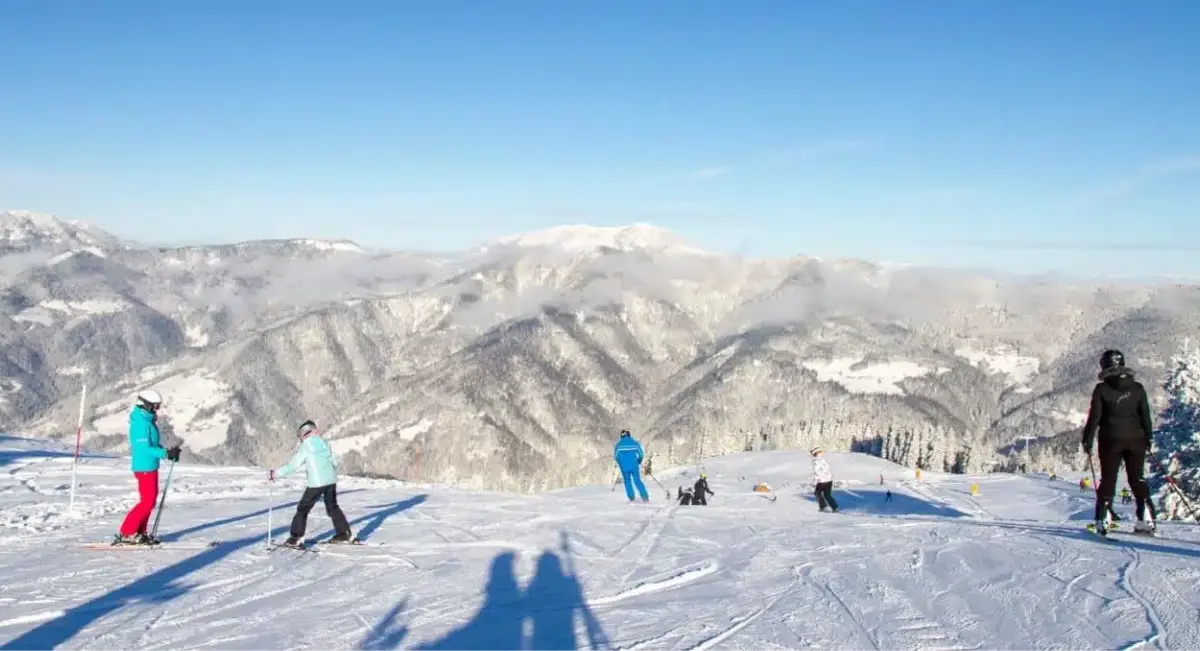 Smučarji na snežni gorski progi s čudovitim razgledom na zasnežene gore in modro nebo.
