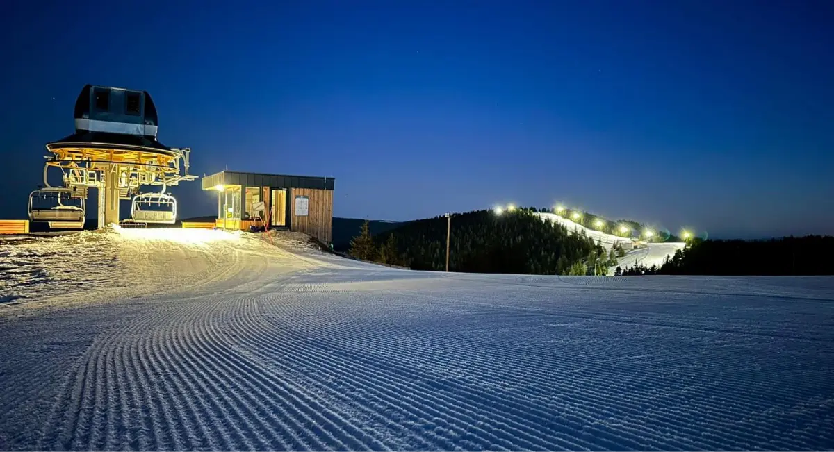 Osvetljeno nočno smučišče z žičnico in gozdom v ozadju