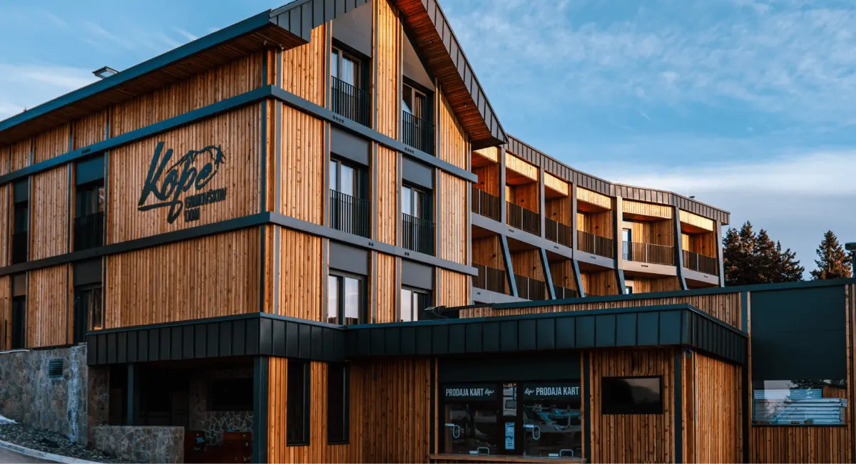Lesena stavba v gorah s sodobno arhitekturo in napisom "Kope" na fasadi.